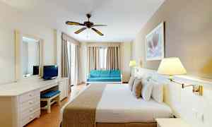 Hotellihuone, jossa on parisänky, kirjoituspöytä, sohva ja kattotuuletin. (Tekoälyn luoma teksti)