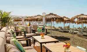 Terassi, jossa istumapaikkoja ja pöytiä, näkymä rannalle, jossa on aurinkovarjoja ja aurinkotuoleja. (Tekoälyn luoma teksti)