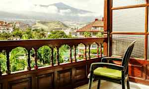 Näkymä parvekkeelta, jossa puurakenteinen kaide, jonka edessä vihreä puutarha ja vuori taustalla. (Tekoälyn luoma teksti)