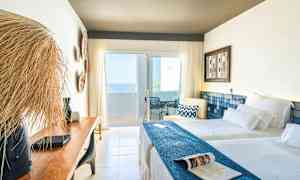 Valoisa hotellihuone, jossa on kaksi vuodetta, puupenkki ja parveke merinäköalalla. (Tekoälyn luoma teksti)