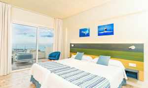 Hotellihuone, jossa kaksi erillistä sänkyä, vihreä ja sininen sängynpääty sekä parveke merinäköalalla. (Tekoälyn luoma teksti)