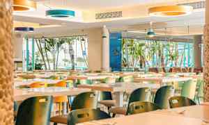 Ravintola värikkäillä tuoleilla ja suurilla ikkunoilla, joista näkyy palmuja. (Tekoälyn luoma teksti)