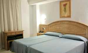 Hotellihuone, jossa kaksi yhden hengen vuodetta sinisillä vuodevaatteilla. Puukalusteet ja seinällä oleva taulu. (Tekoälyn luoma teksti)