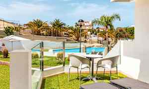 Näkymä terassilta, jossa on aurinkotuoleja, pöytä ja tuoleja, uima-altaalle ja ympäröivään vehreyteen. (Tekoälyn luoma teksti)