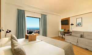 Hotellihuone, jossa on sänky, sohva, kirjoituspöytä ja iso ikkuna, josta on näkymä merelle. (Tekoälyn luoma teksti)