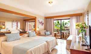 Hotellihuone, jossa on kaksi sänkyä, istuinryhmä ja parveke. (Tekoälyn luoma teksti)