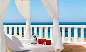 Aurinkovuode valkoisen kattokankaan alla, näkymä merelle, pyyhe ja samppanjajäähdytin. (Tekoälyn luoma teksti)