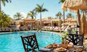 Aamiainen tarjoillaan pöydässä uima-altaan äärellä, taustalla aurinkotuoleja ja aurinkovarjoja. (Tekoälyn luoma teksti)