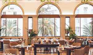 Tyylikkäästi sisustettu ruokasali, jossa on suuret kaari-ikkunat ja näkymä vehreetille puita. (Tekoälyn luoma teksti)