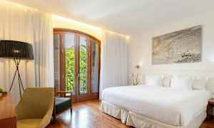 Valoisa hotellihuone, jossa on suuri sänky, puukalusteita ja parveke näkymällä. (Tekoälyn luoma teksti)