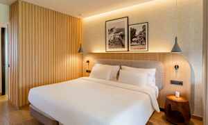 Makuuhuone, jossa on parivuode, puupaneliseinä ja kaksi kehystettyä mustavalkovalokuvaa sängyn yläpuolella. (Tekoälyn luoma teksti)