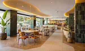 Tyylikäs ravintola, jossa on modernit huonekalut ja sisustus, sisätiloissa vihreitä yksityiskohtia ja suuri baari taustalla. (Tekoälyn luoma teksti)