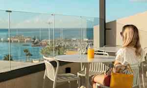 Henkilö istuu pöydässä, jossa on lasi ja kannu appelsiinimehua, näkymä on pienvenesatamaan. (Tekoälyn luoma teksti)