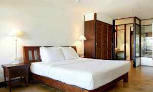 Kuva hotellihuoneesta, jossa suuri sänky valkoisilla vuodevaatteilla, kaksi yöpöytää, pöytälamput ja puiset kaapit. (Tekoälyn luoma teksti)