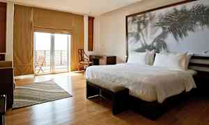 Moderni hotellihuone, jossa on suuri sänky, työpöytä, tuoli ja suuri lasiovi, joka johtaa parvekkeelle. (Tekoälyn luoma teksti)