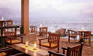 Ulkoterassi meren äärellä, jossa puisia tuoleja ja pöytiä sekä useita valaisevia petroolilamppuja. (Tekoälyn luoma teksti)