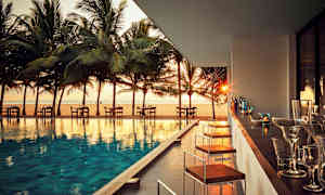 Ulkoterassi uima-altaan äärellä, näkymä rannalle ja palmuja auringonlaskun aikaan. (Tekoälyn luoma teksti)