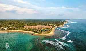 Ilmakuva trooppisesta rantaviivasta, jossa hotelli sijaitsee lähellä rantaa palmuineen ja meren äärellä. (Tekoälyn luoma teksti)