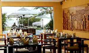 Ravintola, jossa on katettuja pöytiä ja ikkunanäkymä ulkoalueelle ja aurinkovarjoihin. (Tekoälyn luoma teksti)