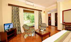 Hotellihuone, jossa istuimet, pöytä ja tv, näkymänä vihreä puutarha. (Tekoälyn luoma teksti)