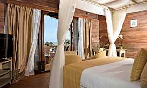 Makuuhuone, jossa puuseinäpaneelit, suuret ikkunat verhoilla ja näkymä merelle. Huoneessa on sänky ja istuma-alue. (Tekoälyn luoma teksti)