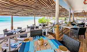 Ulkoterassialue, jossa punotusta bastista tehty katto hiekkarannan ja sinisen meren äärellä. (Tekoälyn luoma teksti)