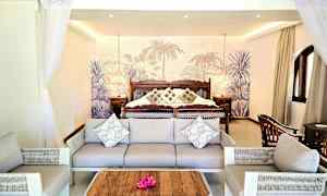 Hotellihuone, jossa sohva ja nojatuolit ison sängyn edessä, koristetyynyjä ja trooppinen tausta. (Tekoälyn luoma teksti)