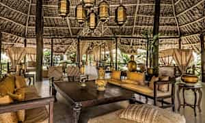 Sisustettu ja koristeltu avoin alue, jossa on puupöytiä, sohvia ja lyhtyjä kauniin olkikaton alla. (Tekoälyn luoma teksti)