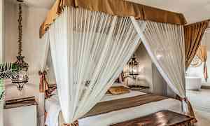 Makuuhuone, jossa on katosvuode valkoisten verhojen ympäröimänä ja lämpimän sävyisillä tekstiileillä sisustettuna. (Tekoälyn luoma teksti)