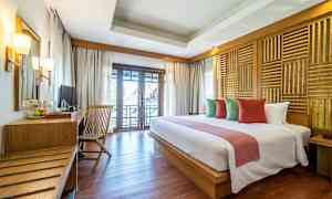 Hotellihuone, jossa on parisänky, erivärisiä tyynyjä, puupöytä ja tuoli sekä parveke näkymällä. (Tekoälyn luoma teksti)