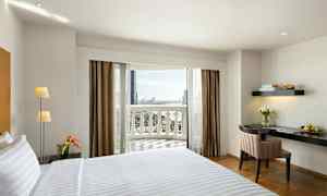 Hotellihuone, jossa on sijattu sänky, kirjoituspöytä ja kukkia sekä parveke näkymineen. (Tekoälyn luoma teksti)