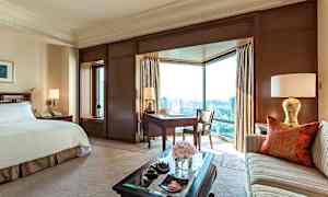 Tyylikäs hotellihuone, jossa on suuri sänky, sohva, työpöytä ja suuret ikkunat näkymällä kaupungille. (Tekoälyn luoma teksti)