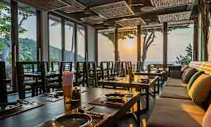 Ravintolan sisätila, jossa katettuja pöytiä ja suuret ikkunat päästävät sisään auringonlaskun valon. (Tekoälyn luoma teksti)