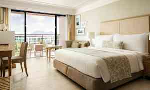 Hotellihuone, jossa on suuri sänky, kirjoituspöytä ja parveke, josta on näkymä. (Tekoälyn luoma teksti)