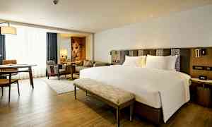 Moderni hotellihuone, jossa on suuri sänky, oleskelutila ja työpöytä. (Tekoälyn luoma teksti)