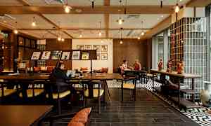 Kahvilan tai työtilan sisustus, jossa puukalusteita, koristeita pöydällä ja ihmisiä työskentelemässä tai keskustelemassa. (Tekoälyn luoma teksti)