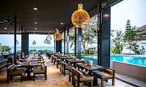 Ravintola ulkona, jossa istumapaikkoja uima-altaan vieressä, taustalla näkyy meri. (Tekoälyn luoma teksti)