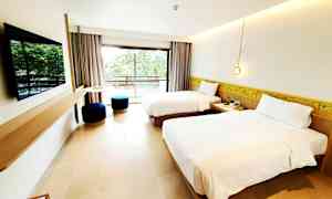 Hotellihuone, jossa on kaksi yhden hengen vuodetta, seinälle kiinnitetty taulutelevisio ja parveke näkymällä vehreyteen. (Tekoälyn luoma teksti)