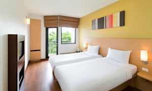 Hotellihuone, jossa on kaksi yhden hengen vuodetta, vaaleat seinät ja ikkuna. (Tekoälyn luoma teksti)