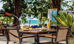 Kattamaton pöytä tuoleineen ulkona, jota ympäröi vehreys, ja taustalla näkyy meri. (Tekoälyn luoma teksti)