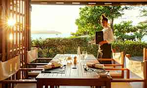 Näkymä ulkoilmaravintolassa katetun pöydän äärellä, taustalla auringonlasku. (Tekoälyn luoma teksti)