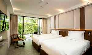 Hotellihuone, jossa on kaksi yhden hengen sänkyä valkoisilla vuodevaatteilla, ikkuna joka avautuu puutarhaan, ja pöytä tuolin vieressä. (Tekoälyn luoma teksti)