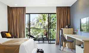 Hotellihuone, jossa on sänky, kirjoituspöytä ja tuoleja sekä näkymä palmuihin lasioven läpi. (Tekoälyn luoma teksti)