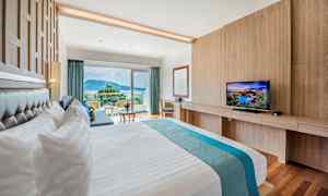 Hotellihuone, jossa on suuri sänky, televisio ja parveke näköalalla ympäristöön. (Tekoälyn luoma teksti)