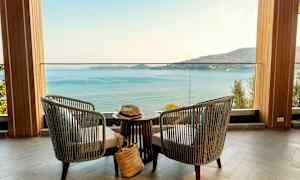 Kaksi tuolia ja pöytä sijaitsevat terassilla, josta avautuu näkymä merelle ja vuoristoiselle rannikolle. (Tekoälyn luoma teksti)