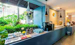 Buffetpöytä, jossa kahvi, kupit, lautaset ja trooppinen vehreys taustalla. (Tekoälyn luoma teksti)