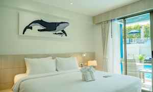 Hotellihuone, jossa on parivuode, koristeltu pyyhkeillä ja seinällä on valaan kuva. Huoneesta on ikkuna, josta näkyy uima-allas. (Tekoälyn luoma teksti)