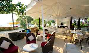 Baari, jossa on tuoleja ja pöytiä rannalla suuren valkoisen katoksen alla. (Tekoälyn luoma teksti)