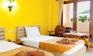 Hotellihuone, jossa on keltaiset seinät, kaksi sänkyä, joissa keltaoranssit päiväpeitteet, ja ikkuna maisemilla. (Tekoälyn luoma teksti)