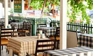 Kuva ravintolasta, jossa on ruudullisia pöytäliinoja ja pöytiä ulkona. (Tekoälyn luoma teksti)